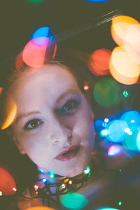 Close-up portrait of young woman with colorful illuminated lights in darkroom