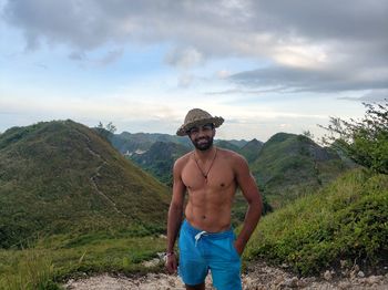 Portrait of shirtless young man standing against mountains