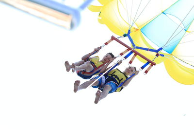 Low angle view of men paragliding against sky