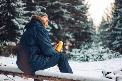 Side view of man sitting on snow covered land