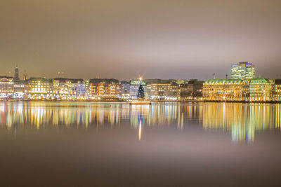 Illuminated buildings by river against sky at night