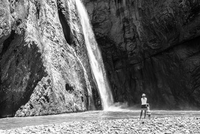 Mother and daughter standing on rock by waterfall