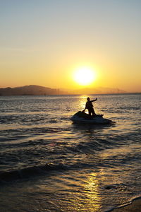 Silhouette man riding in sea against sky during sunset