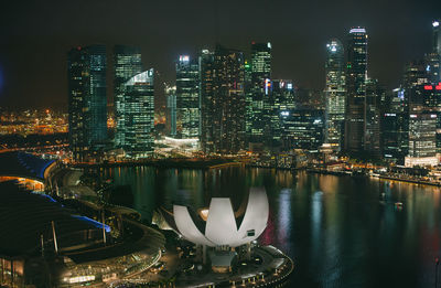 Illuminated buildings by river against sky at night