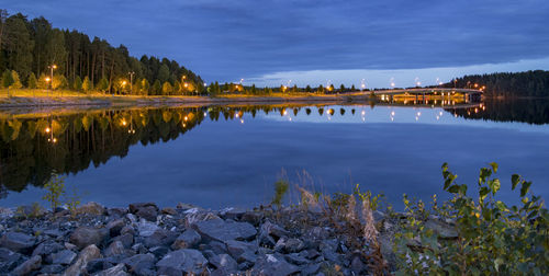 Illuminated street lights reflecting on lake against blue sky