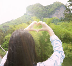 Rear view of woman hand holding heart shape on mountain