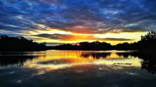 Scenic view of lake against cloudy sky at sunset