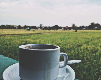 Close-up of coffee cup on field against sky