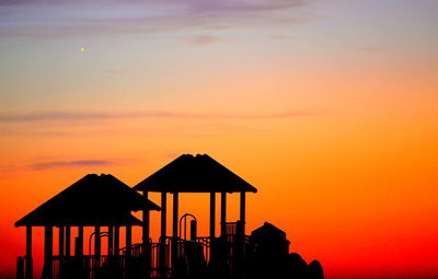 Silhouette built structure on beach against sky during sunset