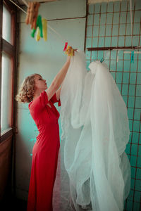 Side view of woman in red dress drying curtain on clothesline