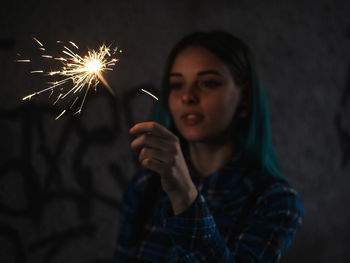 Close-up of young woman holding sparkler at night