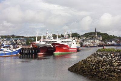 Boats moored at harbor against cloudy sky