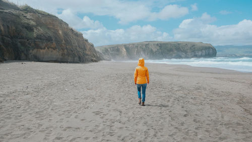 Rear view of woman walking on beach against sky