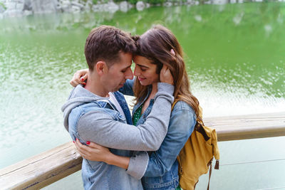 Side view of young woman drinking water while standing against lake