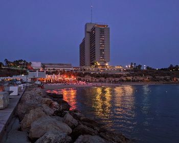 Illuminated buildings by river against sky at night