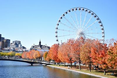 Ferris wheel by river against sky during autumn