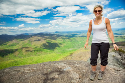 Happy young woman standing on mountain against sky