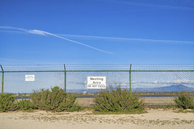 Plants growing on field by fence against blue sky