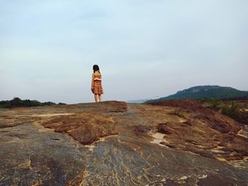 Rear view of woman standing on rock against sky