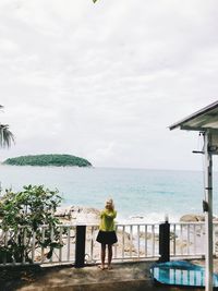 Rear view of woman standing by sea against sky