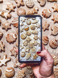 Cropped hand of woman photographing cookies with mobile phone on table