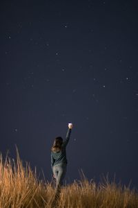 Rear view of young woman with arms raised standing against star field