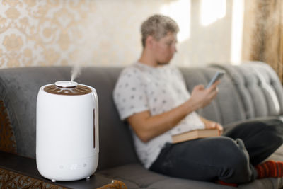 Air humidifier stay in living room. selective focus on vapor. on blurred background caucasian man