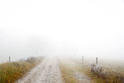 Road amidst field against sky during foggy weather