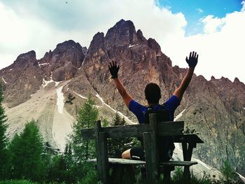 Rear view of man sitting on rock against sky