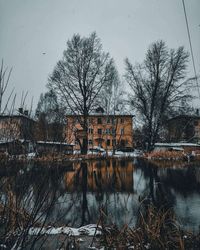 Bare trees by lake against buildings