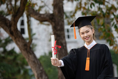 Portrait of smiling student holding diploma while standing outdoors