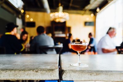 Glass of cocktail on table against people sitting at restaurant