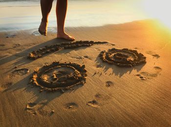 Low section of woman standing by smiley face on shore at beach