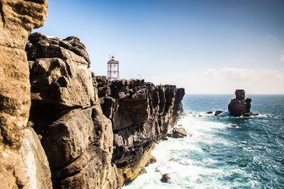 Lighthouse on cliff by sea against clear sky