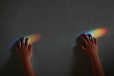 Cropped hands of child touching sunlight falling on wall at home