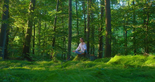 Girl meditating on a green lawn in the forest. treatment of mental illness by practicing yoga.