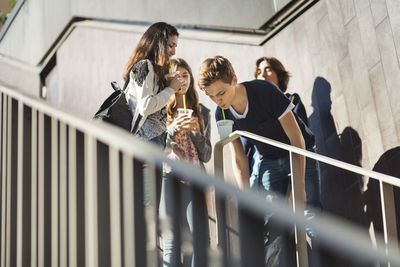 Students looking at friend drinking juice from disposable glass on railing