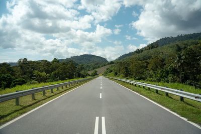 Empty road along trees and plants against sky