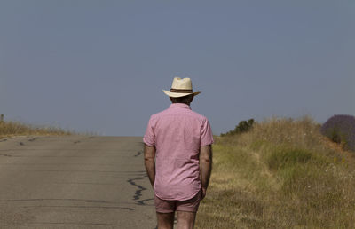 Rear view of adult man in hat walking on country road
