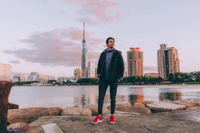 Man standing by river against sky in city