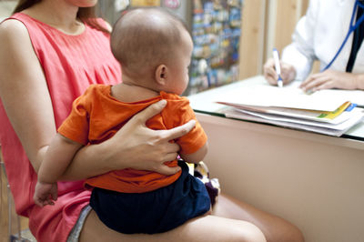 Midsection of mother holding baby girl in clinic