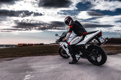 Man riding motorcycle on road against cloudy sky