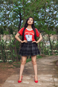 Portrait of beautiful young woman standing on footpath against trees