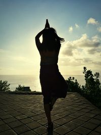 Woman standing by sea against sky during sunset