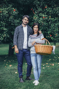 Portrait of couple standing with wicker basket at apple orchard