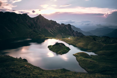Scenic view of lake and mountains against cloudy sky during sunset