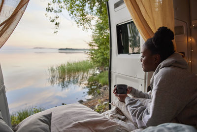 Young woman relaxing in camper van and looking at lake