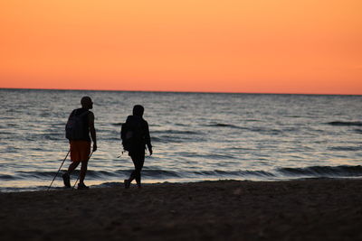 Rear view of men on beach against sky during sunset