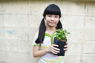 Portrait of smiling girl holding plant against wall