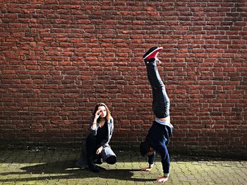 Woman looking at man practicing handstand against brick wall